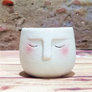 Detailed view of white textured ceramic face flower pot with pink blush accents