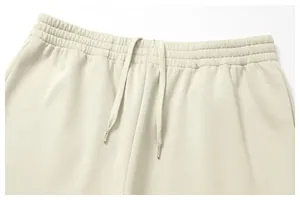 Close-up detail of the elastic waistband and metal-tipped drawstring on beige men's joggers.