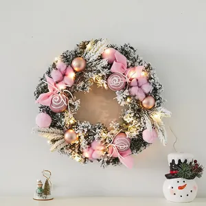 Illuminated Christmas wreath with elegant pink bows and snowy pine needles for festive wall decor