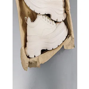 Close-up detail shot of white chunky platform elevator shoes in a craft paper box