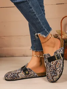 Close-up of paisley print mules with black buckle straps and distressed denim jeans.