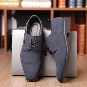 Detailansicht von marineblauen Wildleder-Brogues, die an einem Laptop im Büro lehnen.