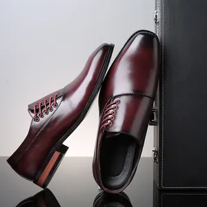Moderne bordeauxrode herenschoenen van leer met vierkante neus tegen een luxe zwarte koffer.