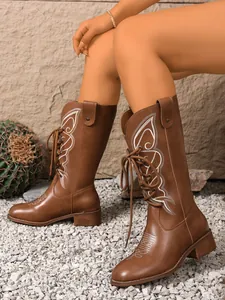 Side view of brown mid-calf boots with white embroidery and lace-up front detail.