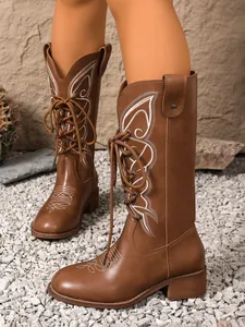 Detailed macro view of brown lace-up tall boots with white butterfly embroidery on model