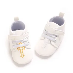 Close-up detail of white PU baby shoes featuring golden cross embroidery and soft soles