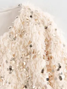 Detailaufnahme einer cremefarbenen flauschigen Jacke mit gold glänzenden Pailletten
