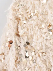 Detailaufnahme von beigem Fransenstoff mit schimmernden Goldpailletten für Damenjacke.