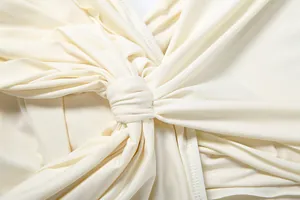 Close-up view of the elegant twisted knot detail on a cream deep V-neck ruched dress.