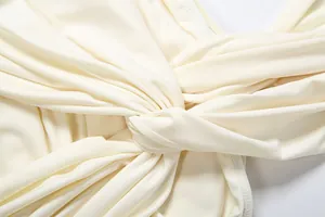 Macro view showing the elegant twist knot and pleat details of a cream sleeveless dress