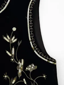 Detailopname van een zwart fluwelen vest met gouden borduurwerk en luxe pailletten.