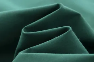 Primo piano del tessuto verde scuro di una camicia casual, consistenza morbida e trama fine.