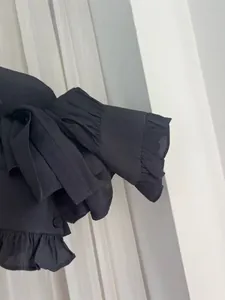 Close-up detail of a black satin blouse featuring elegant ruffle cuffs and textured fabric