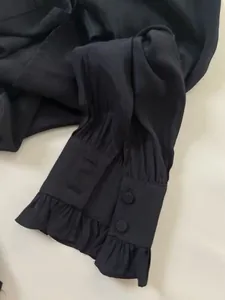 Macro detail of elegant black satin shirt cuff featuring delicate ruffles and double buttons
