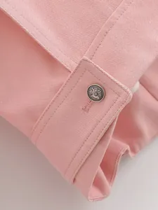 Detailed macro shot of a pink denim jacket cuff featuring an embossed silver button