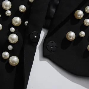 Gros plan des perles blanches irrégulières sur le tissu noir d'une robe blazer.