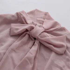 Close-up detail of a soft pink chiffon blouse with a large bow-tie neck design.