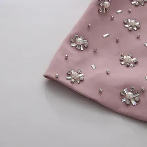 Close-up detail of elegant pink fabric with intricate rhinestone and pearl beadwork.
