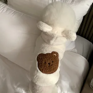 Close-up back view of a dog wearing a white plush pet hoodie with a brown bear patch.