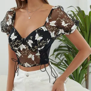 Detalle de top corto de malla negra con bordado de mariposa blanca y mangas abullonadas.
