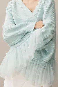 Close-up detail of light blue ribbed knit sweater featuring delicate mesh ruffle layers