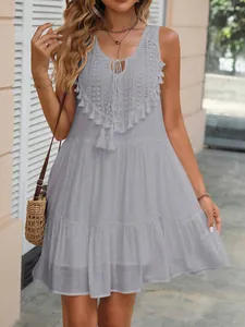 Dettaglio di un abito estivo senza maniche grigio chiaro con pizzo e nappe decorative.