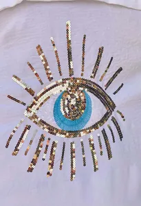 Dettaglio macro del design dell'occhio in paillettes su una camicia bianca casual da donna