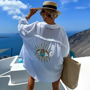 Vista posteriore di camicia bianca con motivo occhio greco in paillettes dorate su sfondo costiero