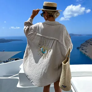 Dettaglio di una camicia in lino beige con motivo Evil Eye in paillettes al mare.