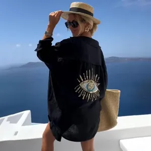Elegante camicia nera da donna con ricamo occhio del male in un suggestivo scenario estivo.
