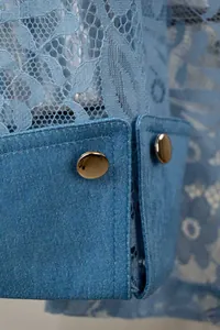 Detailopname van lichtblauwe imitatie denim manchet met kanten patchwork en gouden knopen.