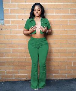 Full body view of a woman in green denim cropped jacket and flared pants set by a brick wall