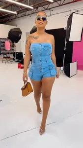 Model wearing a strapless light blue denim romper with button-up front and pockets