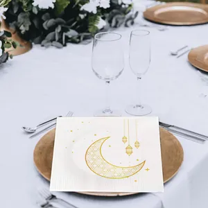 Detalle de servilleta blanca con luna y linternas doradas en un plato de lujo dorado.