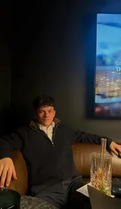 Detail of man wearing a navy knit cardigan with a warm fur collar in a lounge setting.