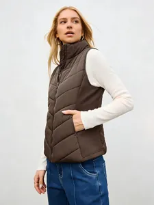 Detail view of a brown stand-collar padded vest worn by a blonde model outdoors.