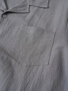 Vista detallada de la textura de la tela y el bolsillo de una camisa de lino gris