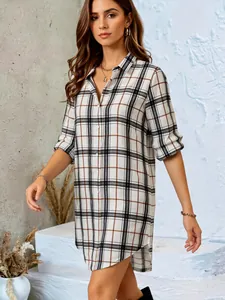 Stylish plaid button-down shirt dress with long sleeves and a flattering curved hemline.