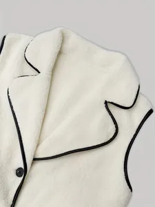 Macro detail of a white sherpa fleece vest featuring a lapel collar and black piping