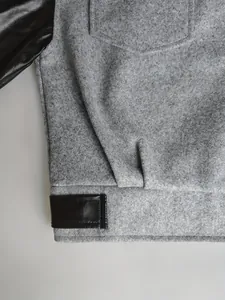 Détail macro montrant la texture du tissu en laine grise et du cuir noir sur une veste bicolore