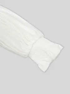 Gros plan d'une manche plissée blanche élégante avec poignet smocké et détails froncés.