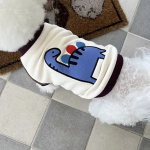 Close-up view of a cream pet sweatshirt with a cute blue dinosaur graphic on a white dog