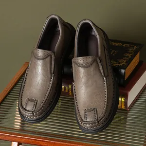 Close-up of men's casual grey leather loafers with stitching details on vintage books.