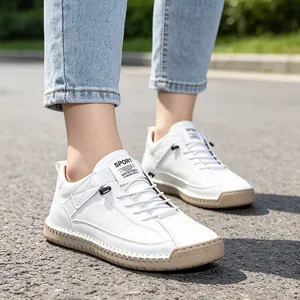 Close-up of white hand-stitched casual women's shoes with tan soles worn outdoors.