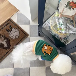 Bichon Frise dog wearing green tiger-print hoodie in a cozy indoor setting