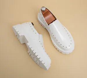 Detailansicht weißer Leder-Brogues mit Goldnieten und dicker Sohle aus hohem Winkel