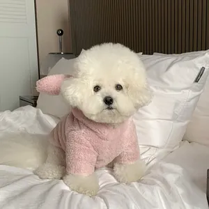Macro view of a Bichon Frise dog in a soft pink fleece hoodie with cute bunny ears on a bed.