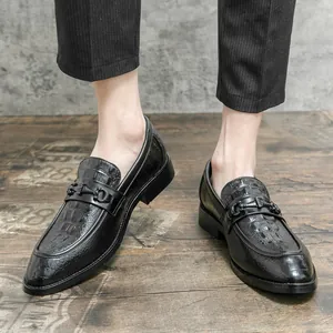 Mocasines negros de hombre con grabado de cocodrilo y detalle de bocado sobre suelo de madera.