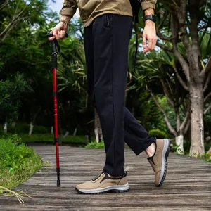 Detail of khaki men's outdoor hiking shoes on a wooden path with a trekking pole