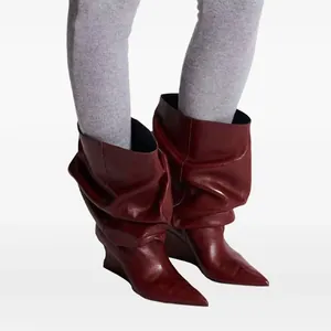 Primer plano de elegantes botas de cuero color burdeos con cuña y diseño de pliegues